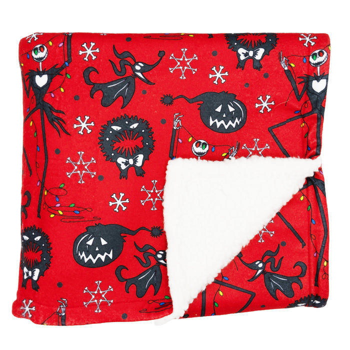 The Sassy Woof Pet Blanket - The Nightmare Before Christmas™ (Red) features black cartoon jack-o’-lanterns, whimsical characters, snowflakes, and Christmas lights on fleece with a white sherpa lining—perfect for the holidays.
