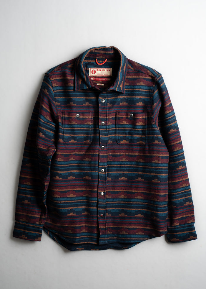 Striped button-up shirt with a geometric pattern in blue and red tones, featuring two chest pockets and a collar.