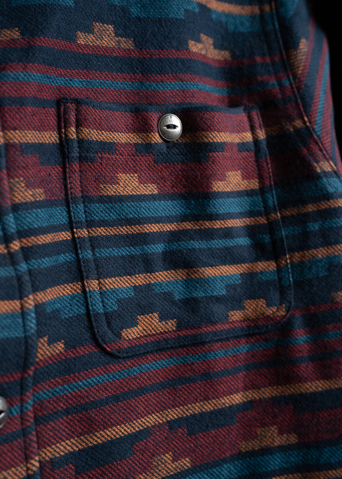Close-up of a patterned fabric with geometric designs in blue, red, and orange, featuring a pocket with a silver button.