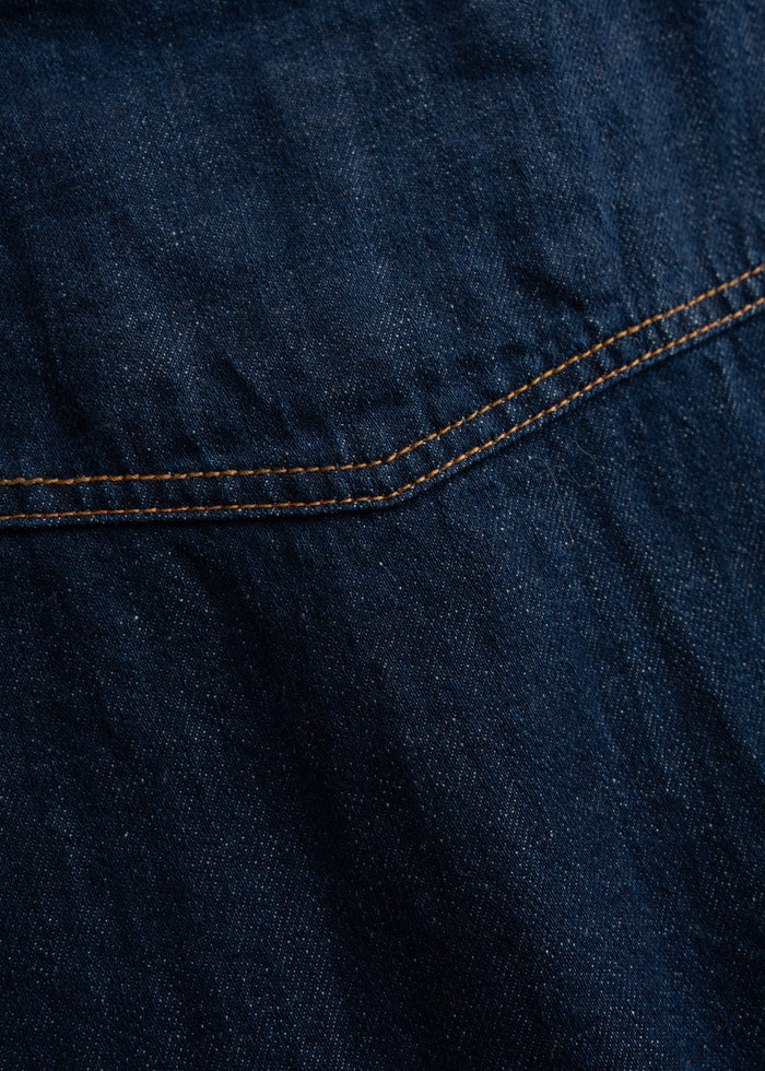 Close-up of dark blue denim fabric with visible stitching, highlighting texture and detail.