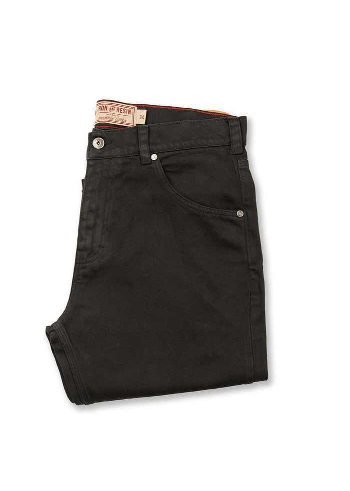 Folded black jeans with Iron and Resin label, showcasing classic design and metal rivets, laid on a white background.