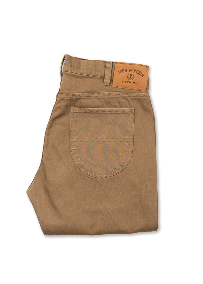 Folded brown pants with a back pocket and a tan leather patch reading "Iron and Resin Denim" on the waistband.