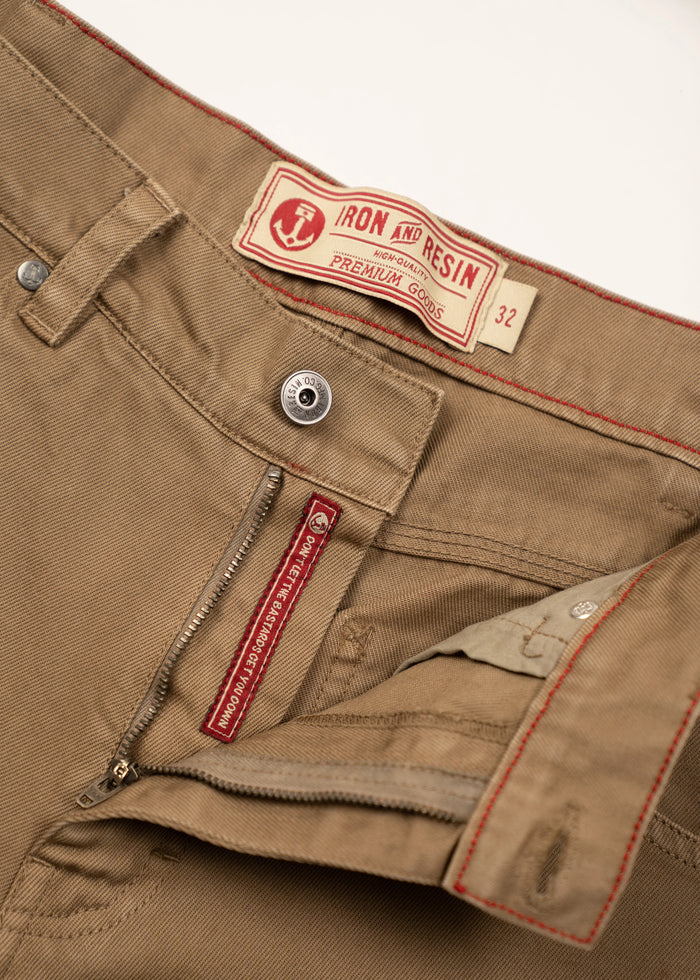 Close-up of khaki pants with Iron and Resin label, size 32. Red stitching accents and zipper detail are visible.