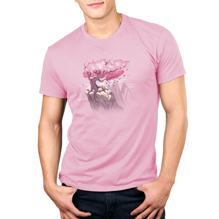 Premium Cotton T-shirt_TeeTurtle Sakura Tree light pink t-shirt featuring an illustration of a pink cherry blossom tree on a rocky cliff with mountains in the background. Blossoms and petals are being blown in the wind.
