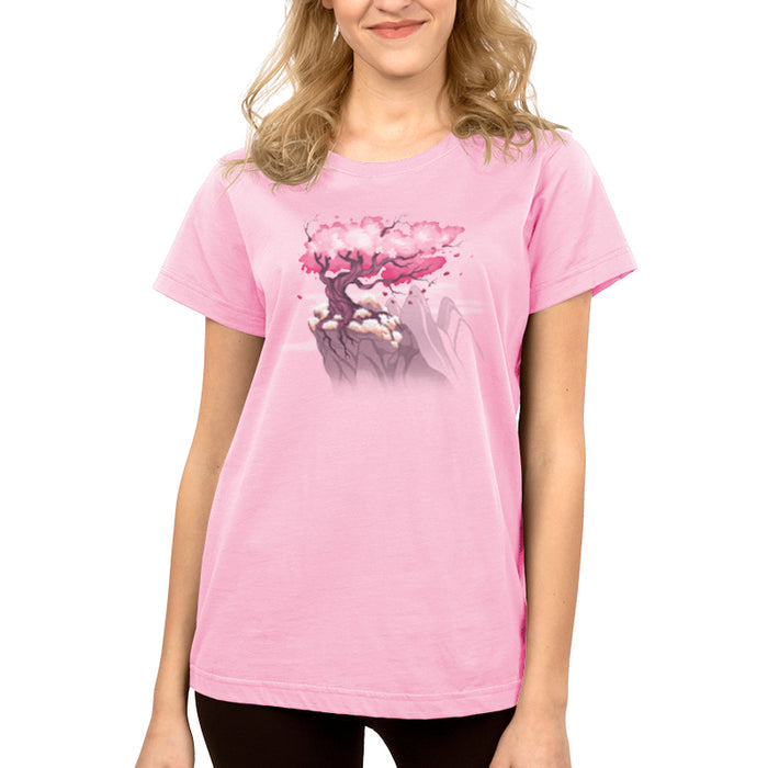 Premium Cotton T-shirt_TeeTurtle Sakura Tree light pink t-shirt featuring an illustration of a pink cherry blossom tree on a rocky cliff with mountains in the background. Blossoms and petals are being blown in the wind.