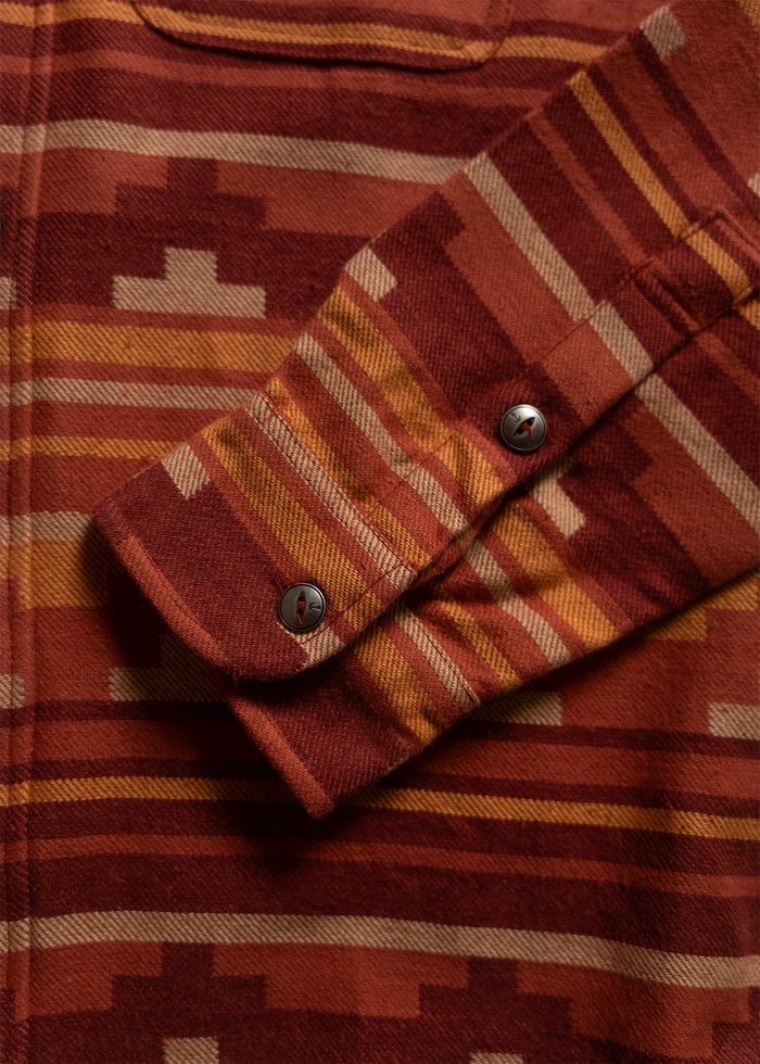 Close-up of a red and orange patterned shirt with geometric designs, focusing on the buttoned cuff detail.