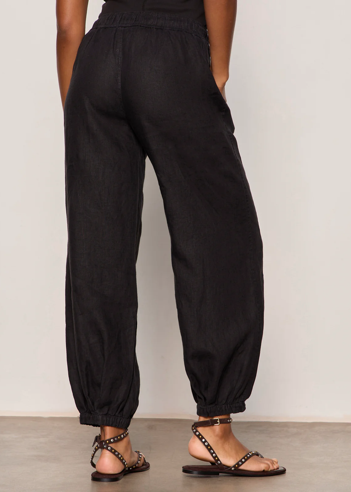 Woman turned around wearing black linen joggers with a black tank top and sandals