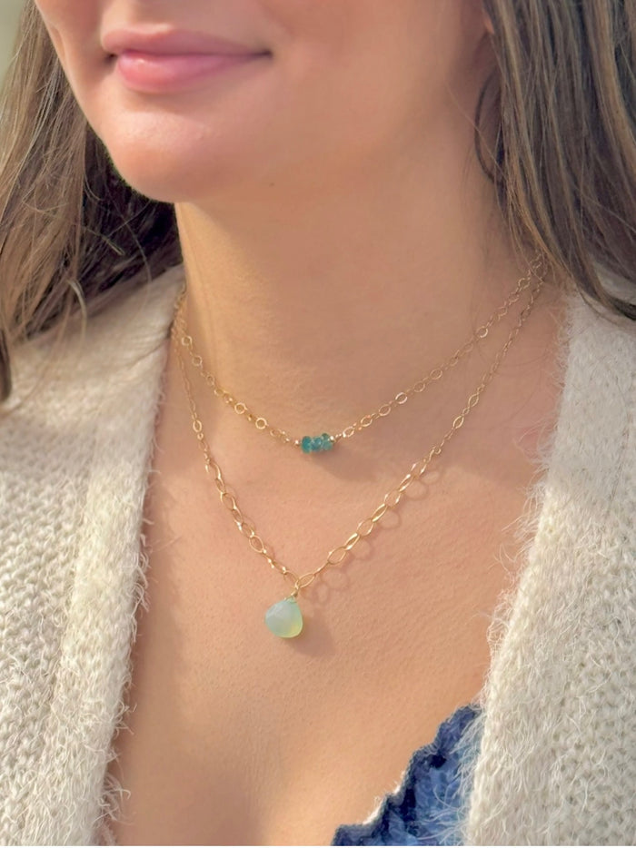 Close-up of a person wearing two gold necklaces with gemstone pendants.