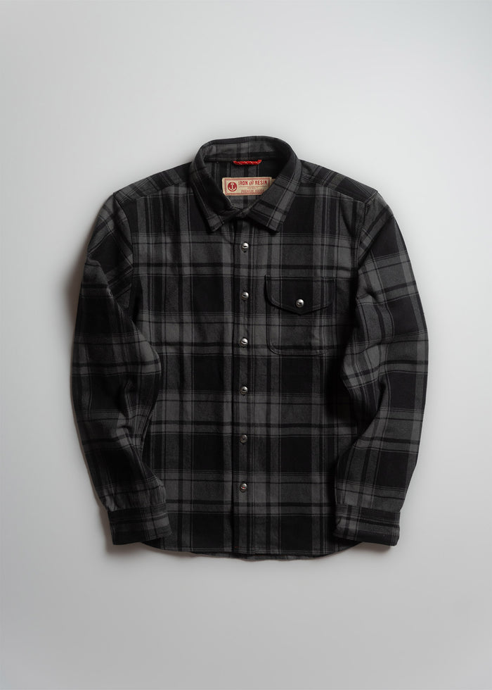 Black and gray plaid flannel shirt with button closure and chest pocket, displayed on a white background.