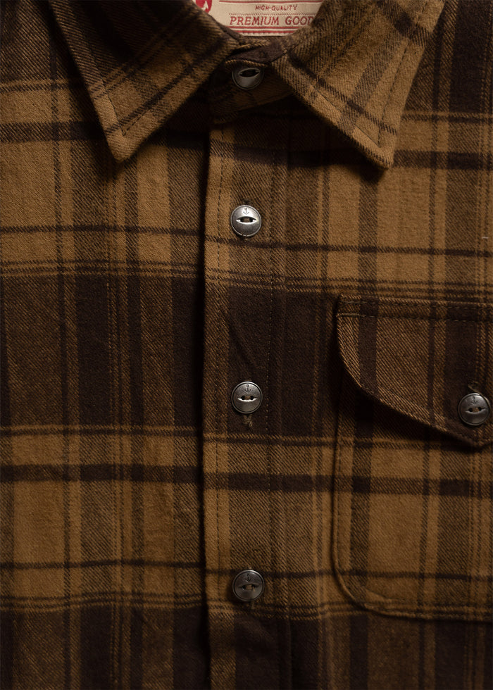 Close-up of a brown plaid flannel shirt with silver buttons and a chest pocket, labeled "Premium Goods" at the collar.