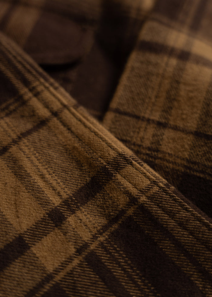 Close-up of brown plaid fabric with intersecting lines, showcasing texture and pattern in warm lighting.