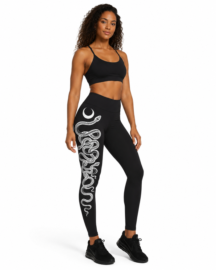 Black snake print leggings with a white serpent and crescent moon art down one leg for yoga, workouts and streetwear styling.