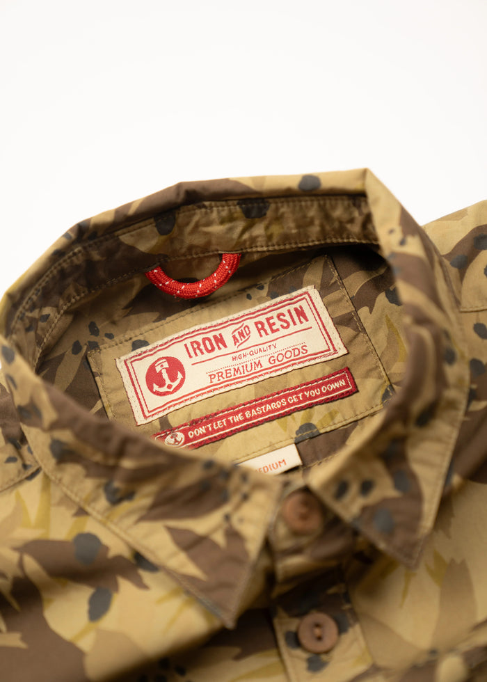 Camouflage shirt with Iron and Resin label, featuring "Premium Goods" and a red loop. Text reads: "Don't let the bastards get you down."