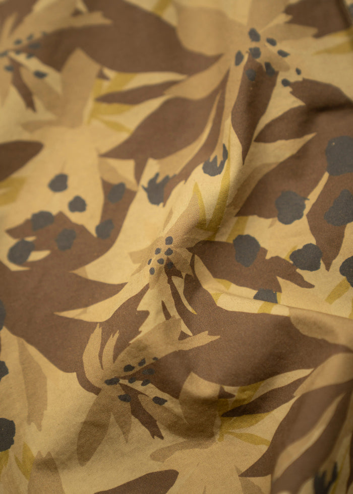 Close-up of brown and beige fabric with abstract floral pattern, featuring dark blue accents and soft folds creating texture.
