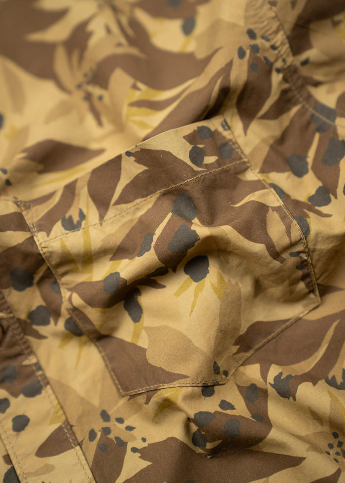 Close-up of a brown and tan camouflage fabric with abstract patterns and visible stitching, creating a textured, rugged appearance.