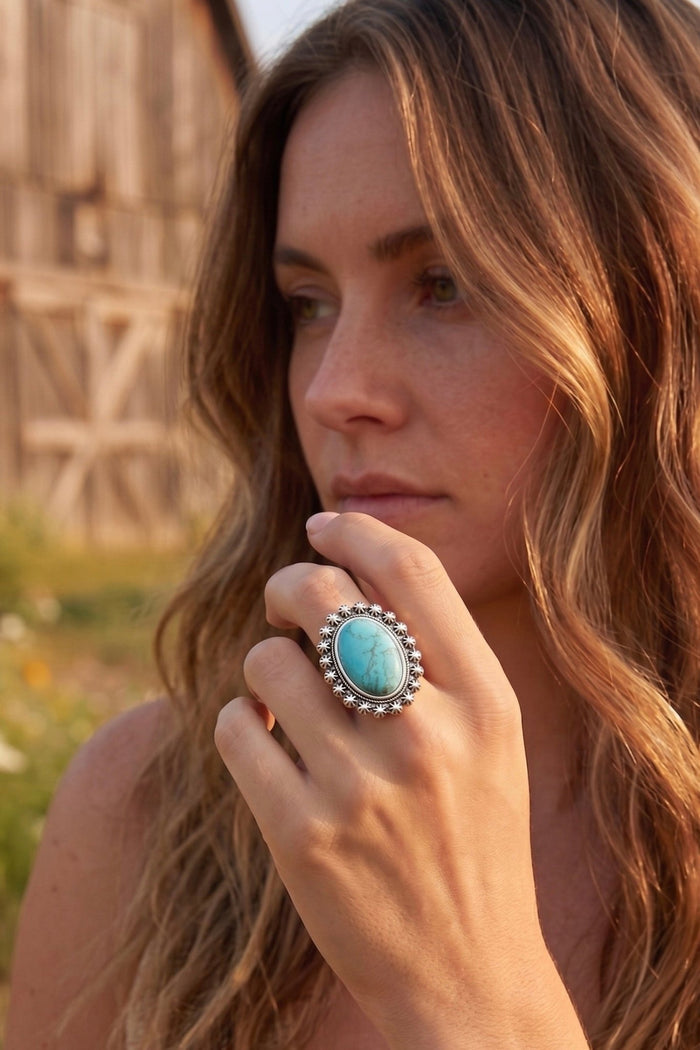 Oval turquoise statement ring with floral silver detailing and adjustable band, styled on hand with a western-inspired antique silver finish.