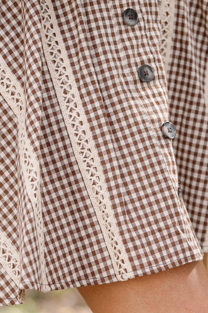 Close-up of the Tash Skort in Hickory Gingham by Ivy City Co, featuring a brown and white checkered pattern with cream lace trim and dark buttons. The decorative cream lace detailing runs between the buttons, enhancing the classic gingham design.