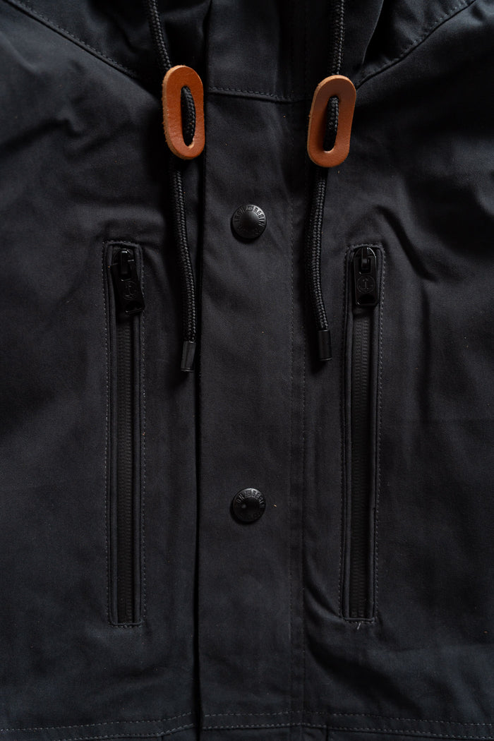 Close-up of a black jacket with brown drawstring toggles, two vertical zippered pockets, and black buttons on the front.