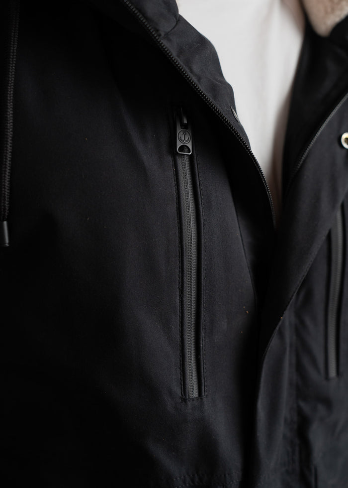 Close-up of a black jacket with a zippered pocket, highlighting sleek design and texture against a white shirt background.