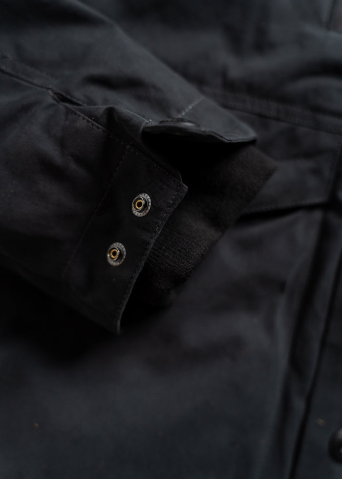 Close-up of a black jacket sleeve with a buttoned cuff and visible stitching, highlighting the fabric texture and design.