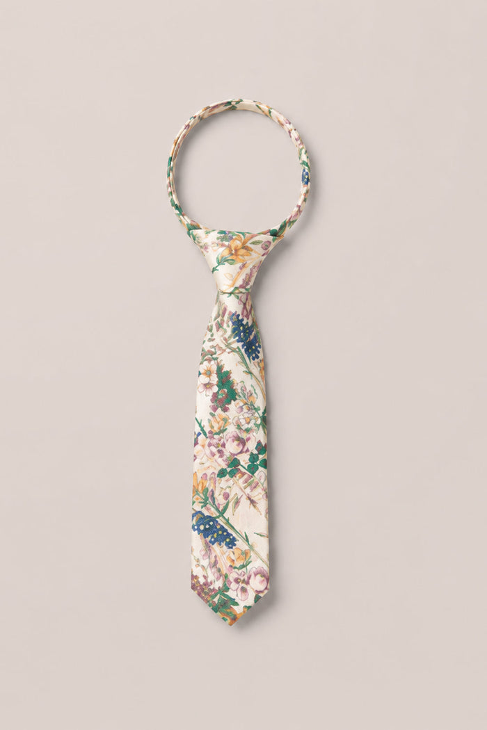 A Ties in Autumn Bouquet tie by Ivy City Co, featuring a floral pattern in green, blue, and pink hues, is laid flat on a light beige background with its loop and knot neatly arranged.