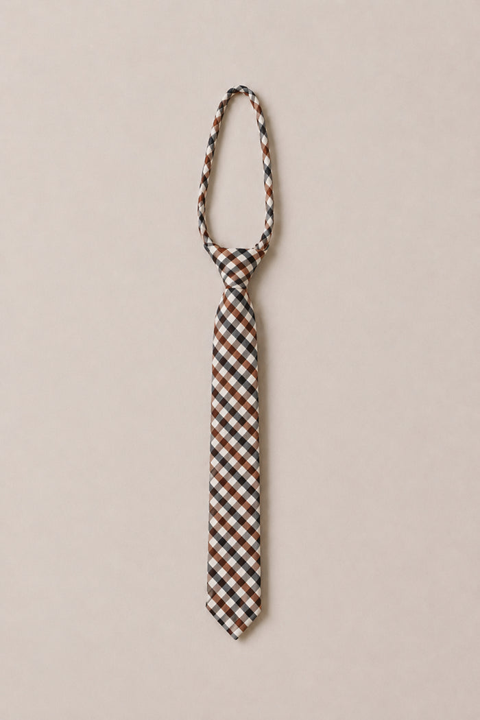 The Ivy City Co Ties in Chestnut Gingham, featuring a classic pattern of brown, black, and white checks, is displayed in a loose knot on a light beige background—an elegant cotton accessory ideal for weddings.