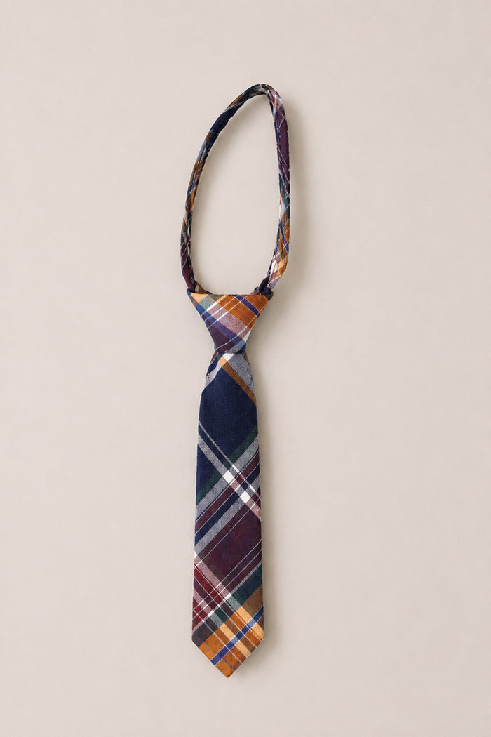 Introducing the “Ties in Midnight Plaid” by Ivy City Co—a sophisticated cotton necktie featuring a striking blend of navy blue, orange, white, and burgundy. Presented against a subtle light beige background, this elegant accessory is an ideal choice for weddings.