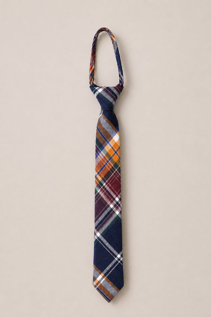 The Ivy City Co Ties in Midnight Plaid, a pre-tied necktie crafted from soft cotton and showcasing navy blue, orange, white, and burgundy stripes, is laid flat on a beige background—perfect for adding a timeless touch to family photos.