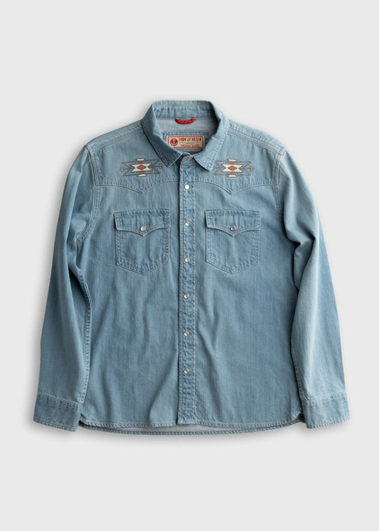 Light blue denim shirt with embroidered geometric patterns on shoulders, buttoned front, and two chest pockets on a plain background.