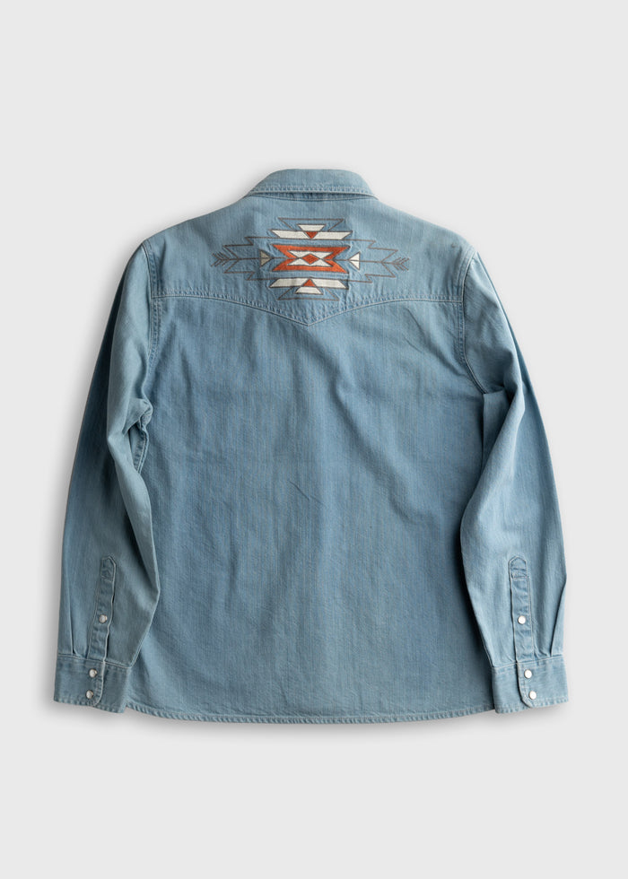 Denim shirt with geometric embroidery on the back, featuring orange and gray patterns, laid flat on a light gray background.