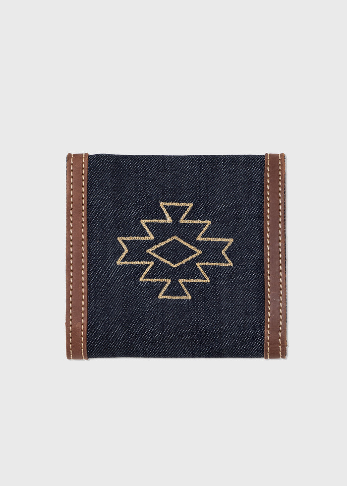 Denim wallet with brown leather trim, featuring a geometric embroidered pattern on the front, set against a plain background.