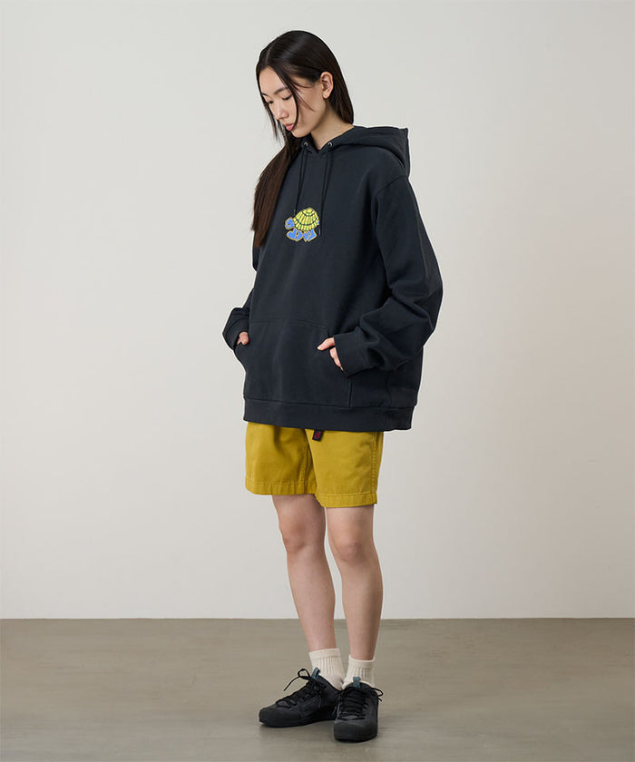 Model wearing a vintage black Gramicci Turtle Hooded Sweatshirt with a turtle graphic and yellow shorts on a light tone background.