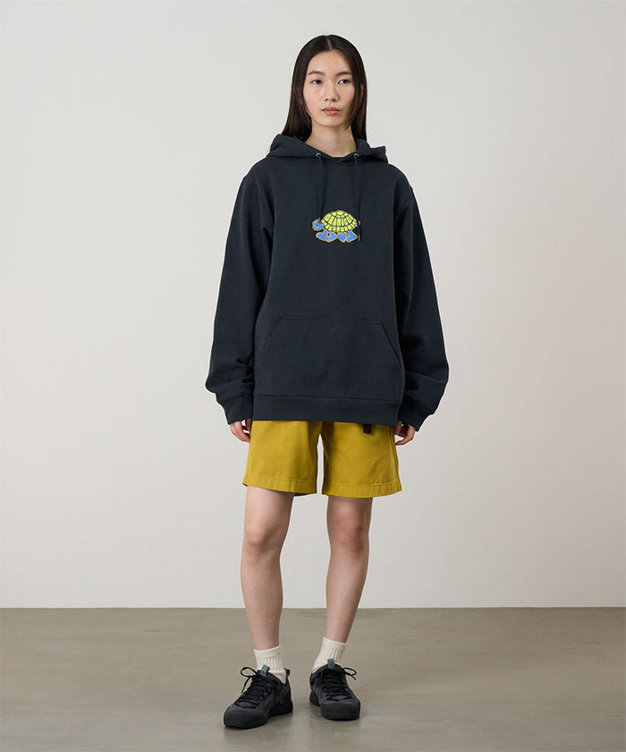 Model wearing a vintage black Gramicci Turtle Hooded Sweatshirt with a turtle graphic and yellow shorts on a light tone background.