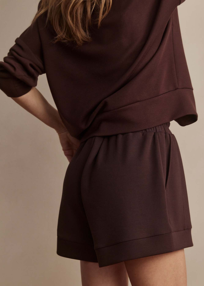 Woman turned to the side wearing brown drawstring shorts with a matching quarter zip sweatshirt