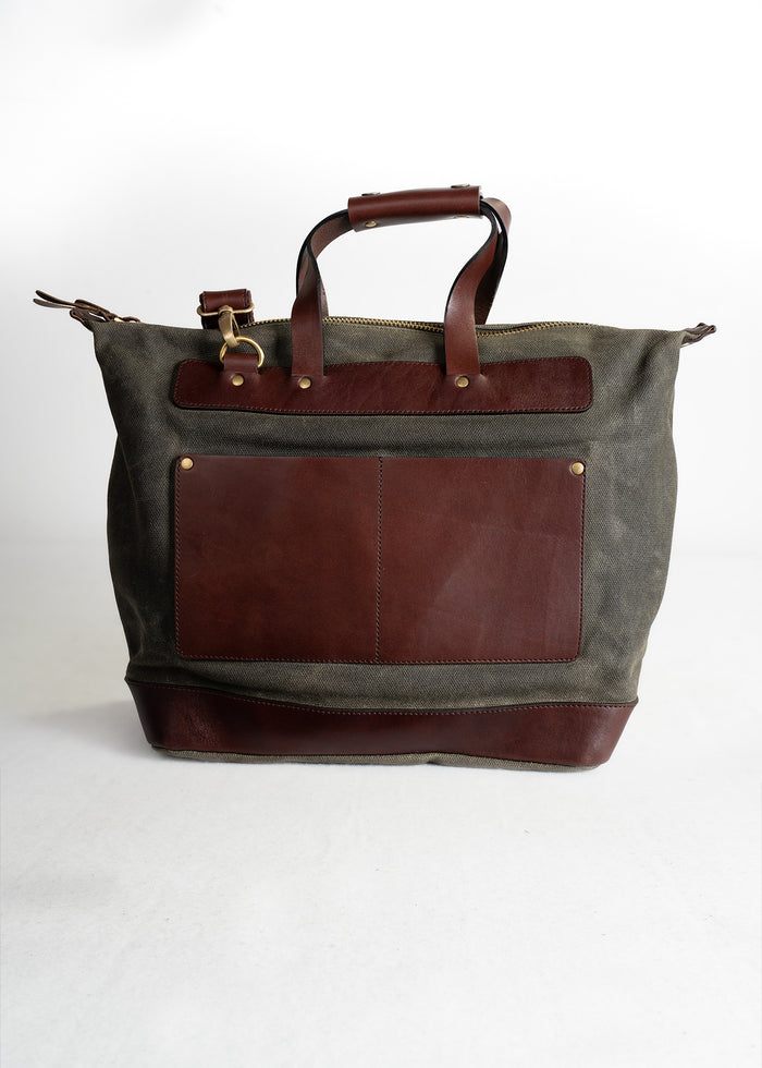 Stylish canvas tote bag with brown leather accents, featuring sturdy handles and a front pocket, set against a plain backdrop.