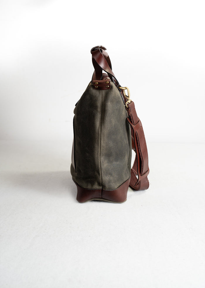 Side view of a brown leather and canvas bag with a strap, set against a plain white background.