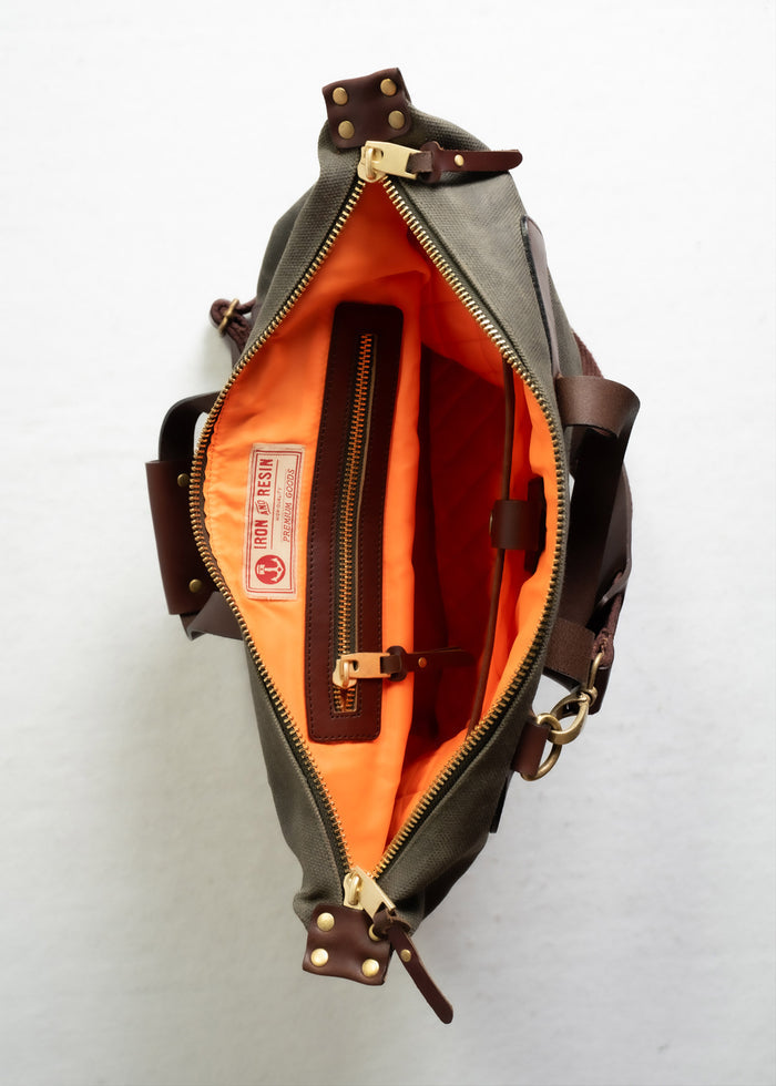 Open olive bag with bright orange interior, leather straps, and a zippered pocket, showcasing craftsmanship and style.