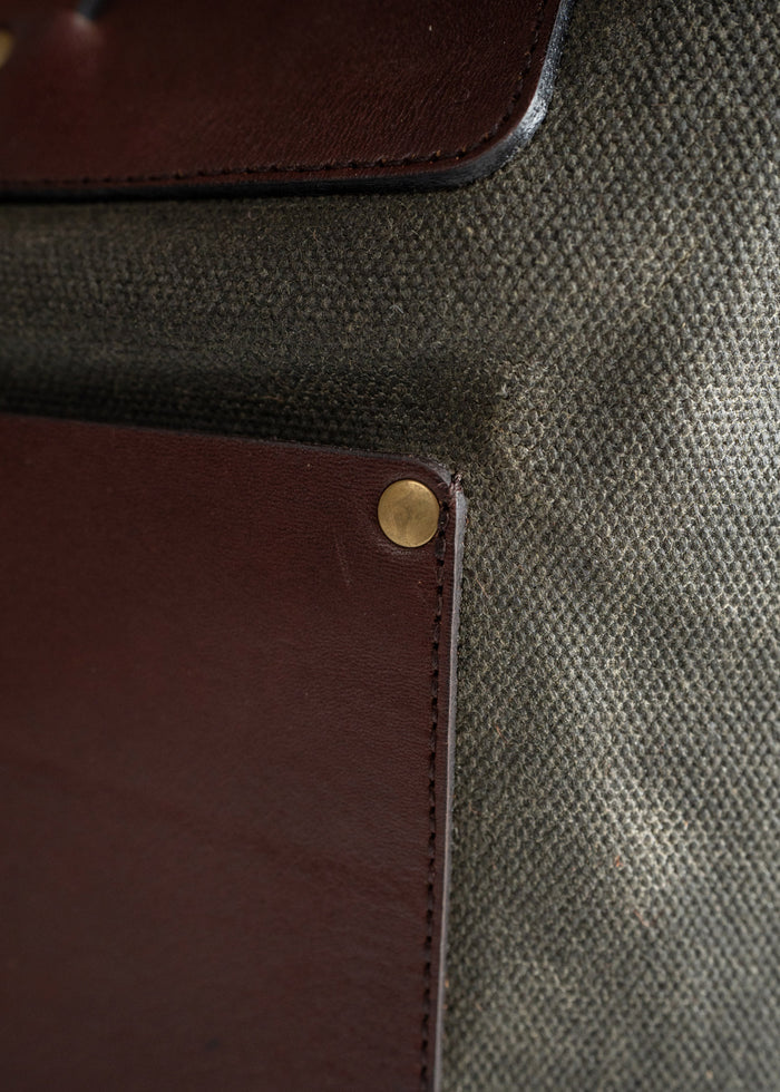 Close-up of a brown leather patch with a brass rivet on textured gray fabric, highlighting material contrast and detail.