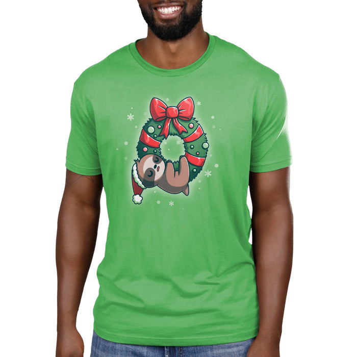 Premium Cotton T-shirt_TeeTurtle We Wish You a Lazy Christmas apple t-shirt featuring a cartoon sloth in a Santa hat, snoozing while hanging from a festive wreath adorned with red ribbons and ornaments.
