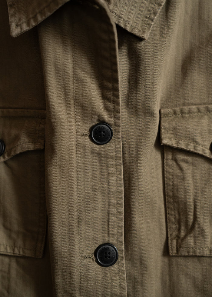 Close-up of a khaki jacket with black buttons and two front pockets, highlighting the texture and stitching details.