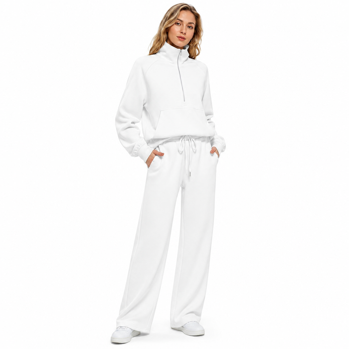 A woman modeling a matching white lounge set consisting of a cropped half-zip sweatshirt and wide-leg sweatpants, paired with white sneakers, against a solid white background.