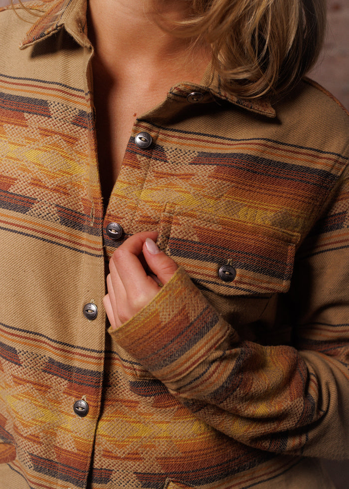 A person wearing a patterned, button-up jacket with warm tones, holding the collar. The focus is on the jacket's texture and design.