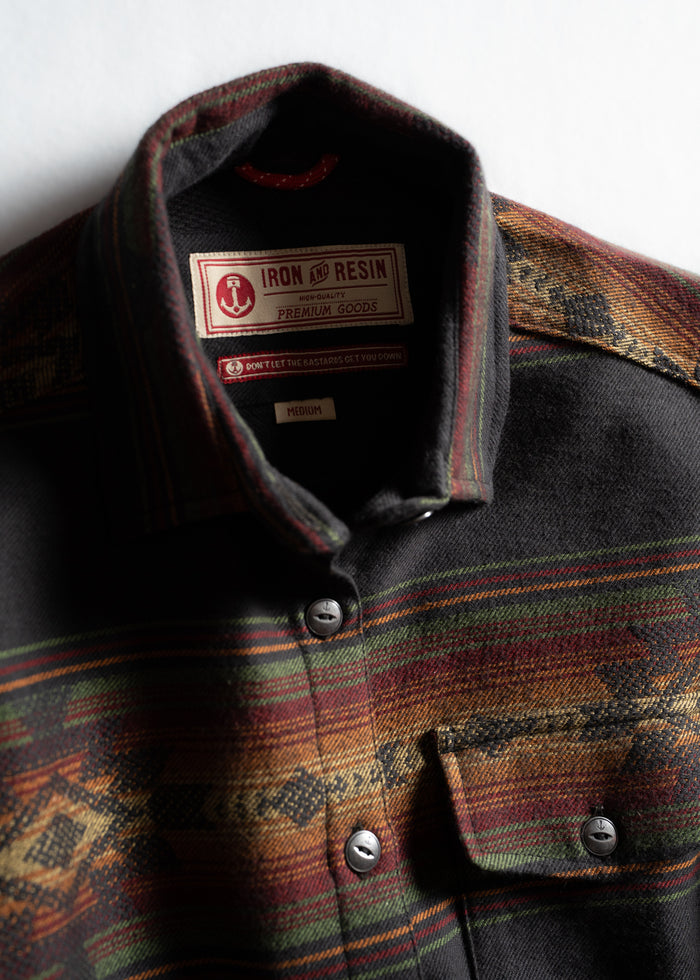 Plaid shirt with Iron and Resin label, featuring earthy tones and metal buttons, highlighting premium craftsmanship and style.