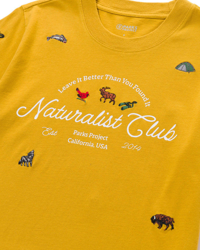 Front close-up of the mustard tee showing Parks Project label at the neckline and small embroidered wildlife along the chest