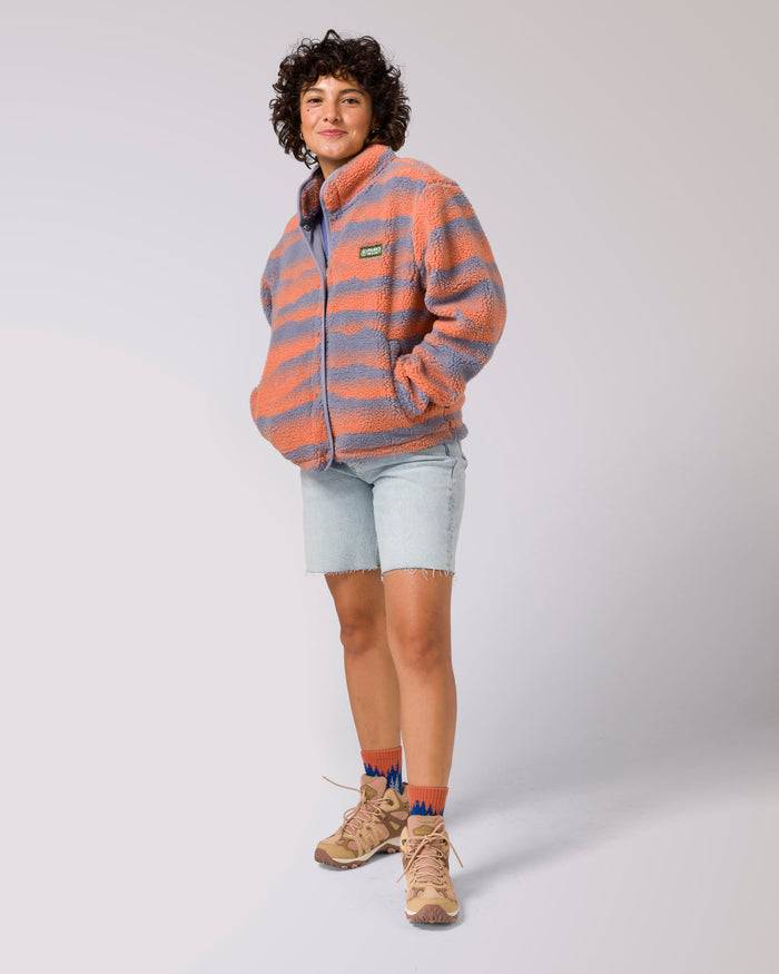 Model in coral and gray striped fleece jacket with Parks Project patch on chest, smiling with arms out.