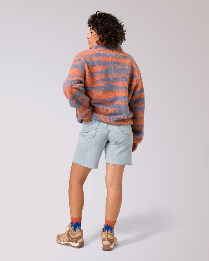 Back view of a model wearing the orange and lavender striped high pile fleece jacket with light denim shorts