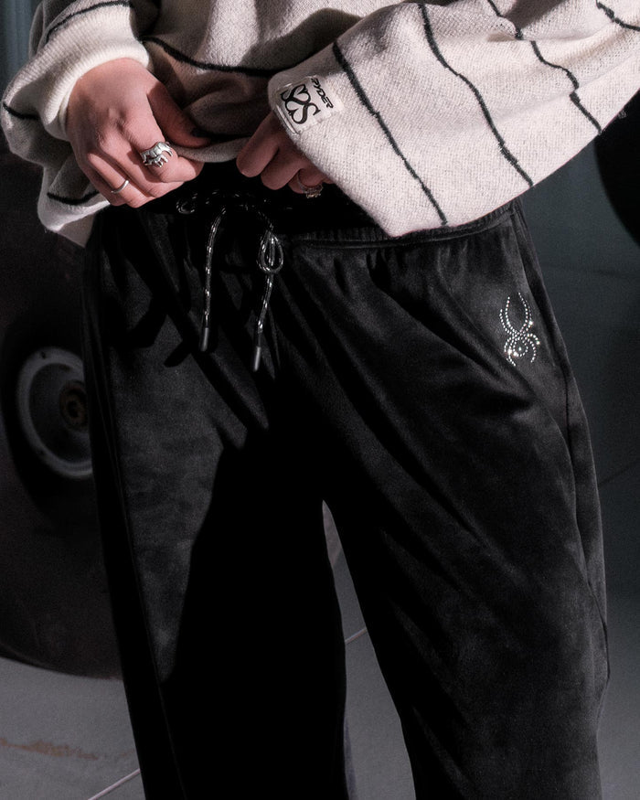 Person wearing black pants with a brand logo, standing next to a skateboard.