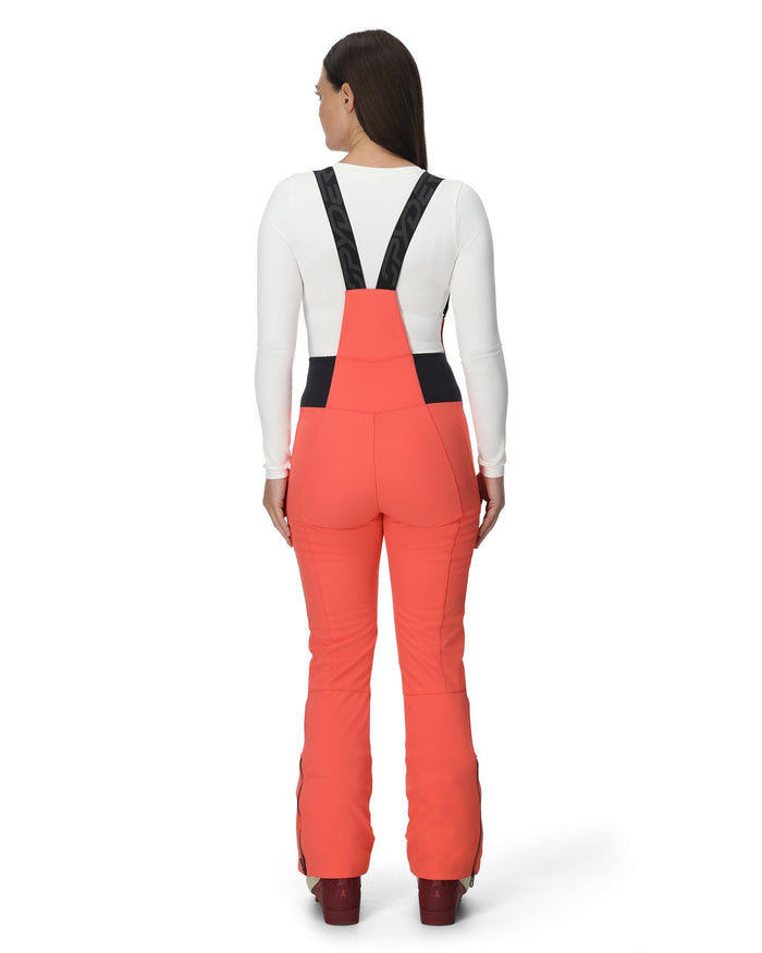 Person wearing coral bib overalls with black straps on a white background