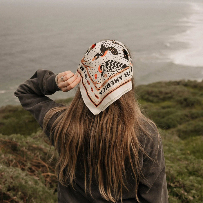 Person wearing a Woodpecker Bandana as a head scarf outdoors with a windy cloudy backdrop