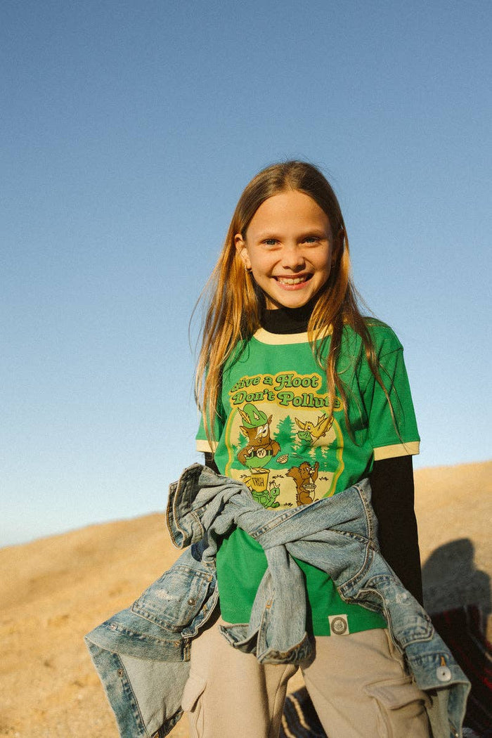Girl in a green Woodsy Owl and Friends youth ringer tee outdoors with a denim jacket tied around her waist.